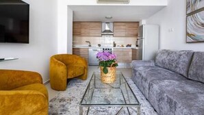 Un salon moderne avec un canapé, des fauteuils, une table basse et une cuisine en arrière-plan.