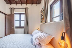 A bedroom with a bed, a window, curtains, a wall-mounted light, and a painting. - Stroumpi Private Pool Villa (Stroumpi)
