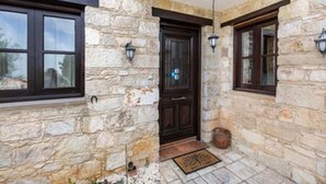 Fachada de pedra com uma porta de madeira escura, duas janelas com molduras escuras e um lustre pendurado.