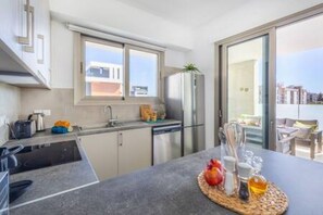 A modern kitchen with a built-in dishwasher, a large window, and a dining area with a table set for two. - 101 Mulberry Court - Spacious with Large Terrace (Agios Athanasios)