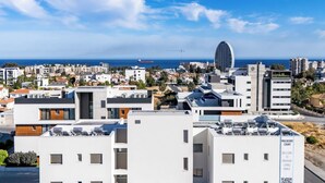 Un paysage urbain moderne, avec une grande roue bien visible, un ciel d’un bleu éclatant et une vue sur la mer.