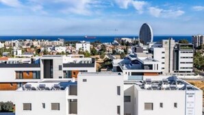 Un paysage urbain côtier avec des bâtiments modernes, une structure circulaire imposante et une vue dégagée sur la mer.