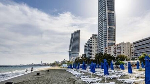 Une plage avec des transats et des parasols, un rivage sablonneux et de grands immeubles en arrière-plan.