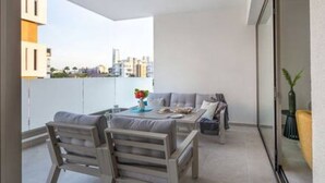Un balcon avec un canapé, deux fauteuils, une table avec un vase et une plante en pot.