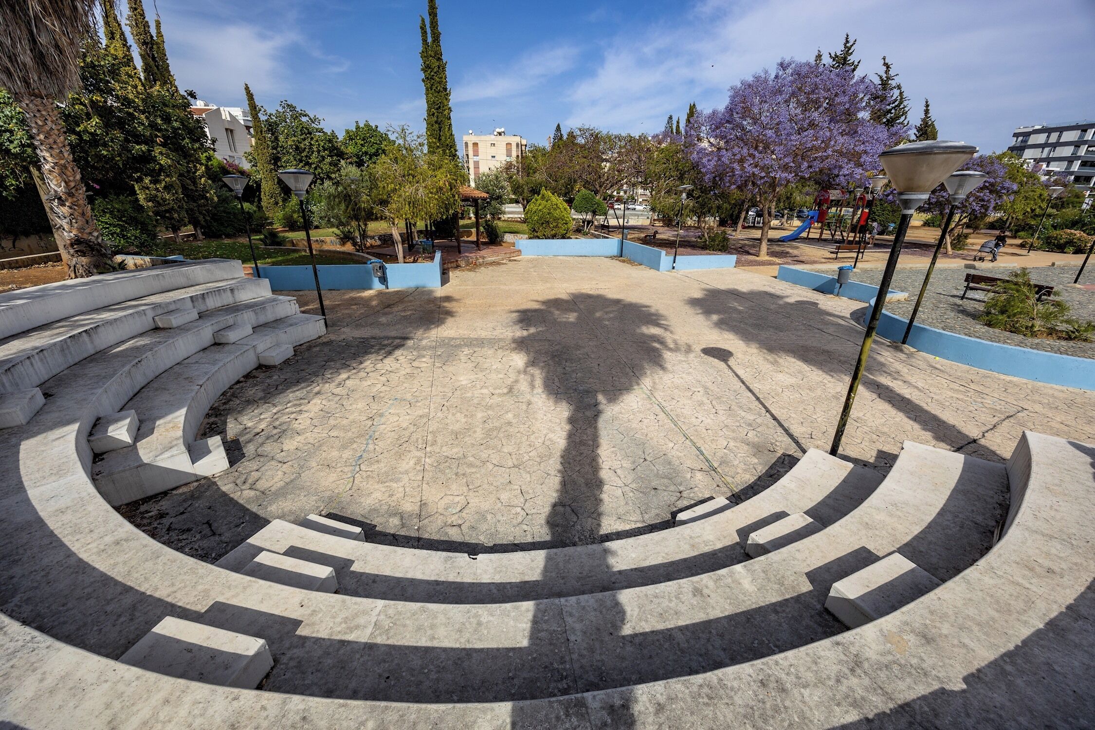 Un espace de détente extérieur circulaire, avec des marches menant à cet espace, entouré d’arbres et avec une aire de jeux en arrière-plan.