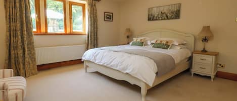A bedroom with a bed, two bedside tables, a window with curtains, a radiator, and a painting on the wall.