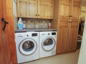 A laundry room with two front-loading washing machines, wooden cabinets, and a tiled backsplash. - Sheephouse Farm (Bacup)