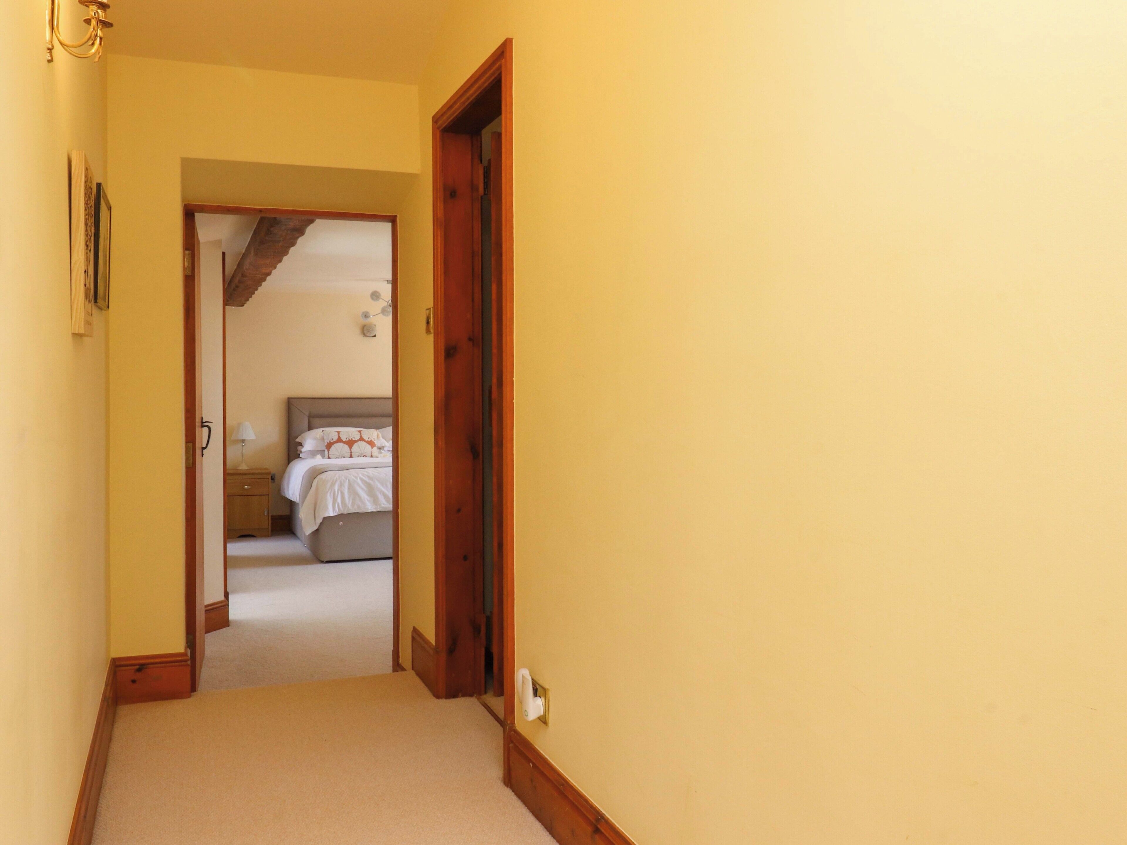 A hallway leading to a bedroom with a bed, a nightstand, and a lamp.
