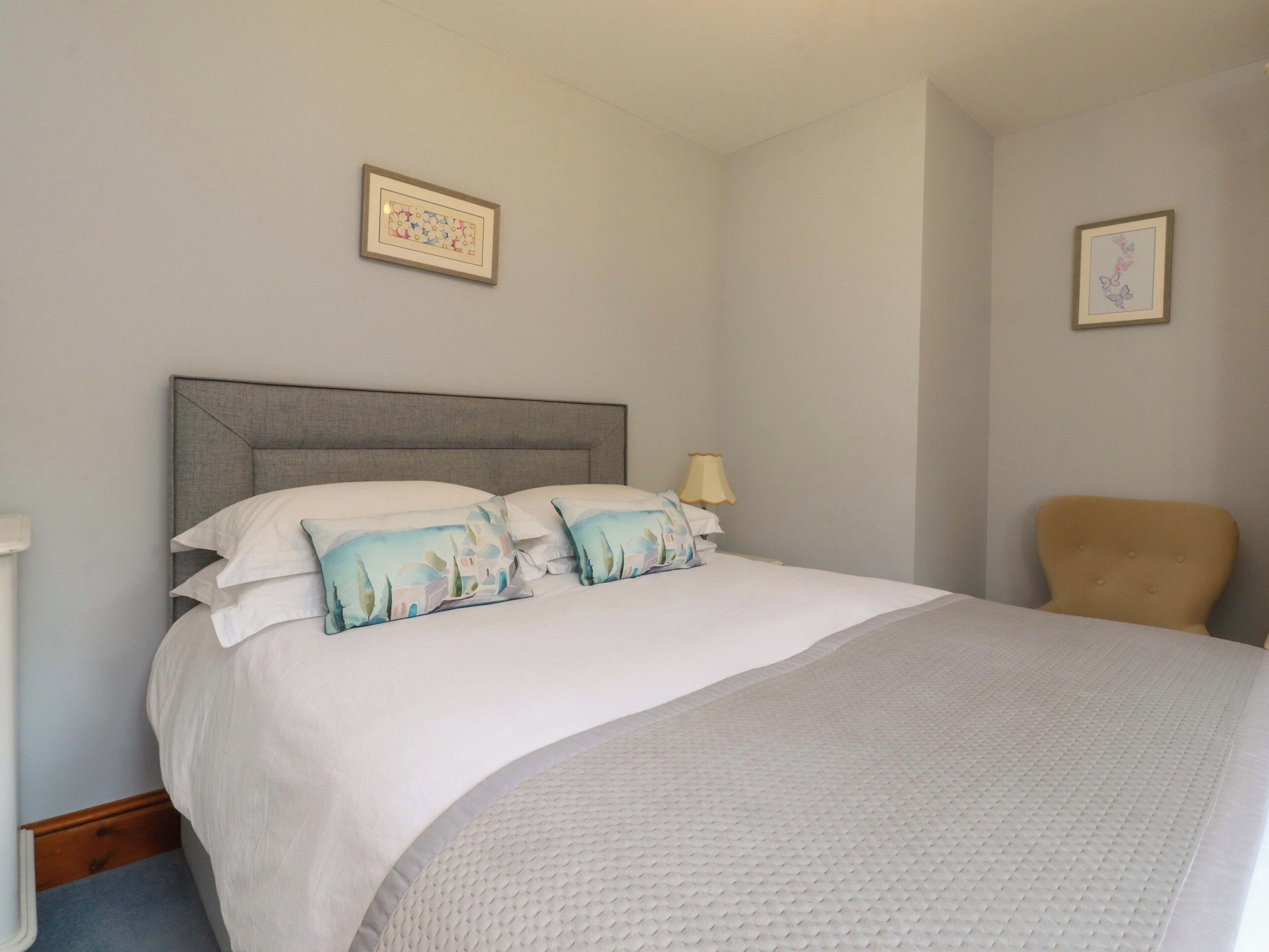 A neatly made bed with a grey headboard, a bedside lamp, and two framed pictures on the wall.