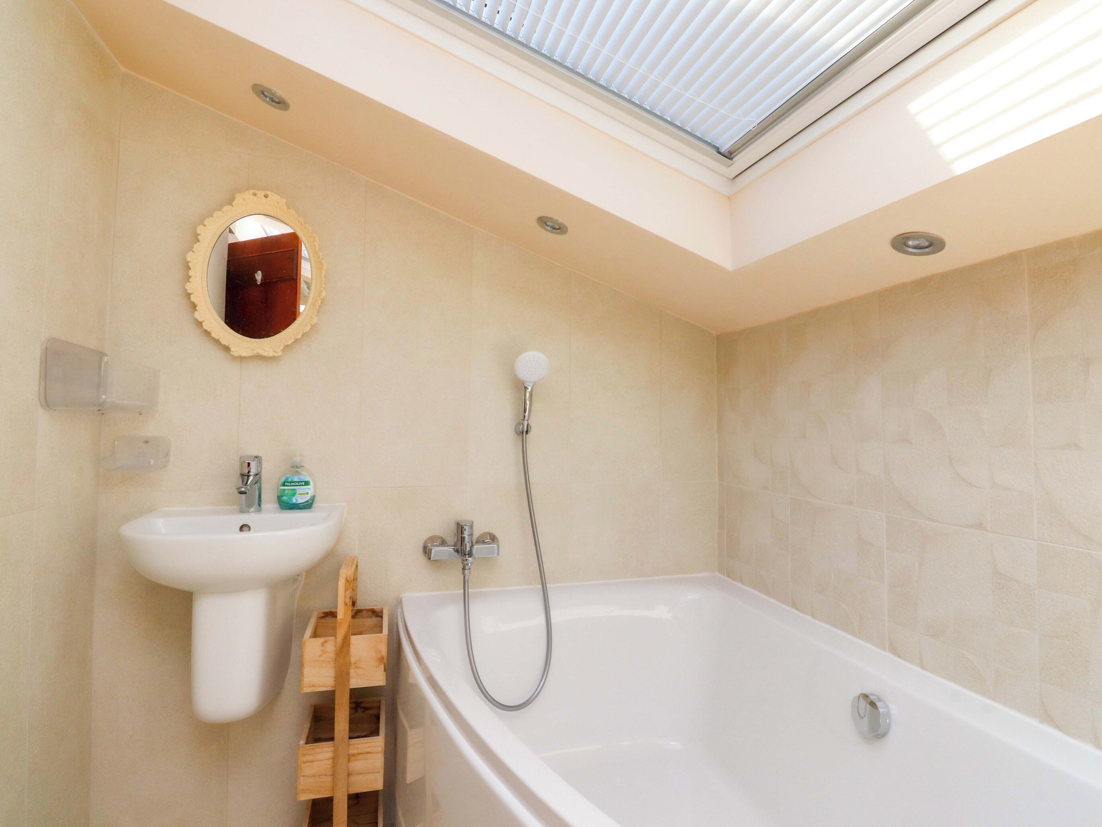 A modern bathroom with a skylight, a freestanding bathtub, a sink, and a wooden storage unit.
