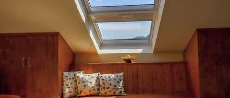 A room with a sloped ceiling, wooden paneling, a bench with cushions, and skylights.