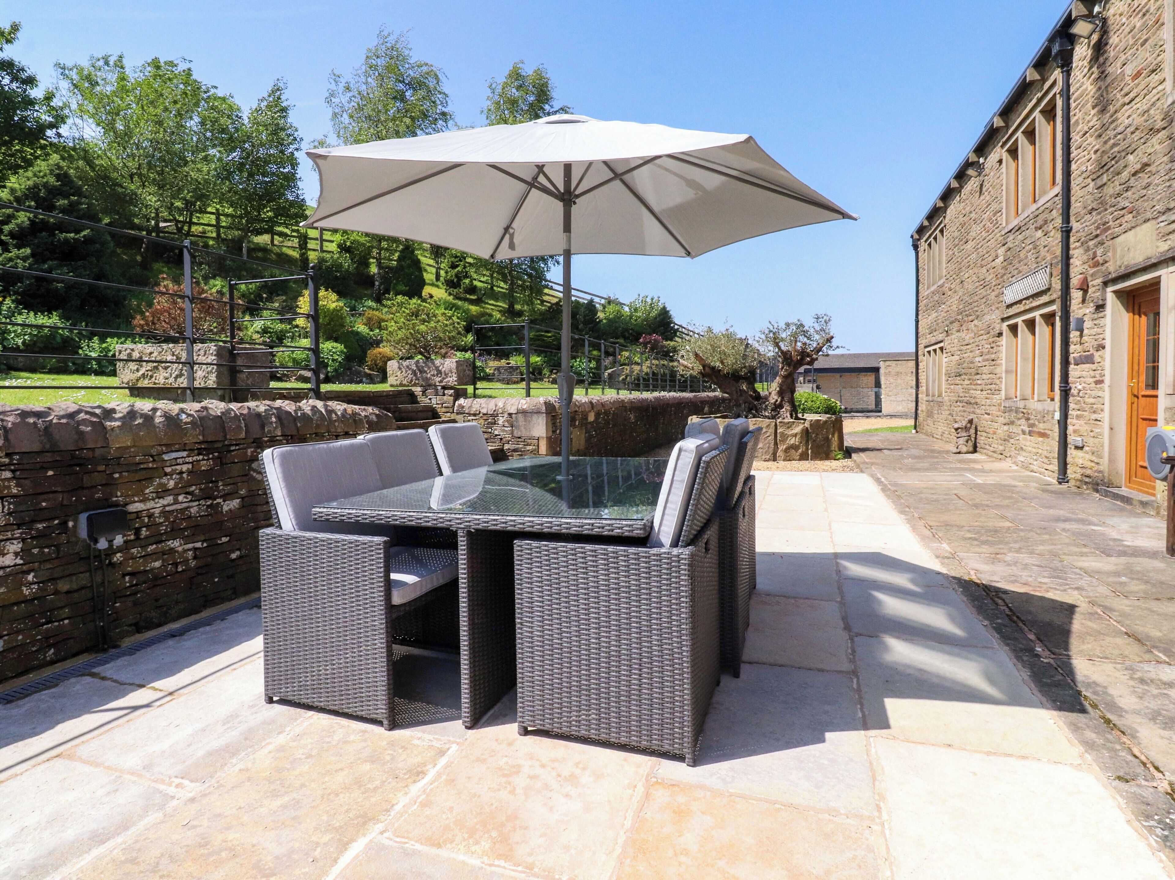 An outdoor patio with a glass-top table and chairs, a large umbrella, stone walls, and a stone building in the background.