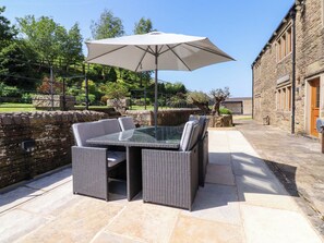 Un patio al aire libre con una mesa y sillas de superficie de vidrio, un paraguas grande, paredes de piedra y un edificio de piedra al fondo.