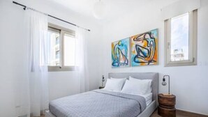 Ein Schlafzimmer mit einem Bett, einem Fenster mit Vorhängen und zwei abstrakten Bildern an der Wand.