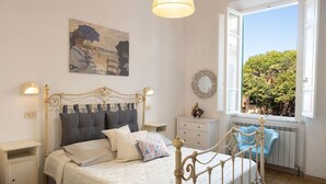 A bedroom with a bed, bedside lamps, a window with a view, a wall-mounted mirror, and a painting. - Tower Hotels (Viareggio)
