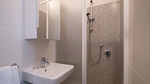 A bathroom with a white sink, a mirror, and a shower with a tiled wall. - Tower Hotels (Viareggio)