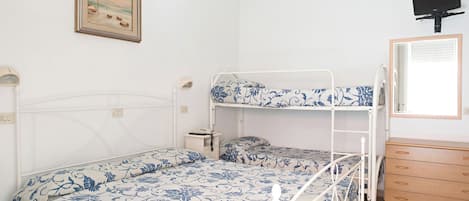 A room with bunk beds, a bedside table, a lamp, a framed picture on the wall, and a TV mounted on the wall.