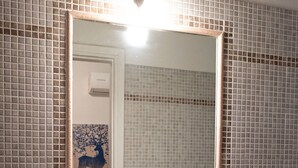 A bathroom with a white sink, a mirror, and a tiled wall. - Tower Hotels (Viareggio)