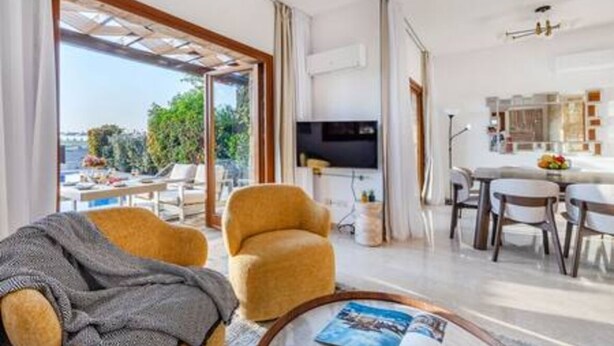 Uma sala de estar moderna com sofá, poltrona e uma área de jantar com cadeiras e mesa.