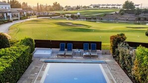 Piscina com espreguiçadeiras, campo de golfe ao fundo e céu claro.