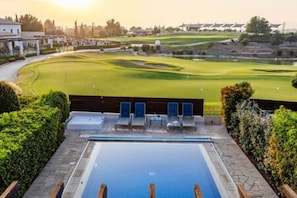 Ein Schwimmbecken mit Liegestühlen, im Hintergrund ein Golfplatz und ein klarer Himmel.