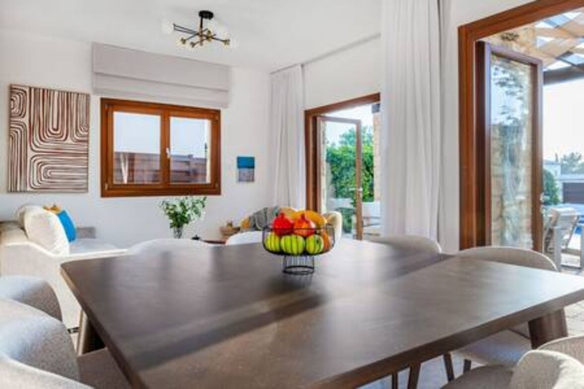 A dining area with a table, chairs, a fruit bowl, and a view through a glass door.