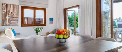 A dining area with a table, chairs, a fruit bowl, and a view through a glass door.