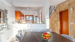Uma cozinha moderna com armários brancos, uma mesa de jantar de madeira e uma tigela de frutas, além de uma parede de pedra.
