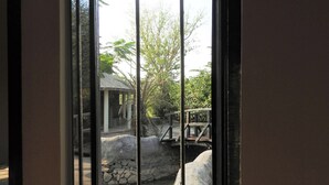 A view through a glass door with a stone wall, a small bridge, and a pond. - Eco Hamlet Farmstay (Mawal)