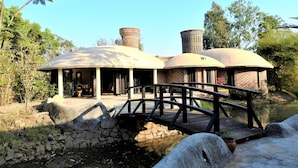 A building with a dome-shaped structure, a brick chimney, and a stone bridge over a water body. - Eco Hamlet Farmstay (Mawal)