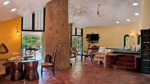 A spacious living area with a glass table, seating, a brick pillar, and a television. - Eco Hamlet Farmstay (Mawal)