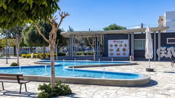 A pool area with a bench, a covered seating area, and a building with a sign. - Olga Apt 4 - lovely studio on ground floor (Limassol)