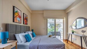 Ein Schlafzimmer mit Bett, Nachttisch, Lampe, Kunstwerk und Blick ins Freie.