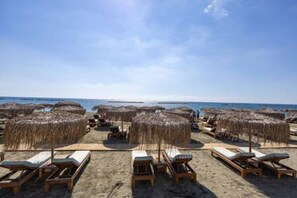 A beach with sun loungers and thatched umbrellas.