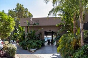 A hotel entrance with a sign reading 'PETITE PLAGE,' surrounded by lush greenery and a paved walkway.