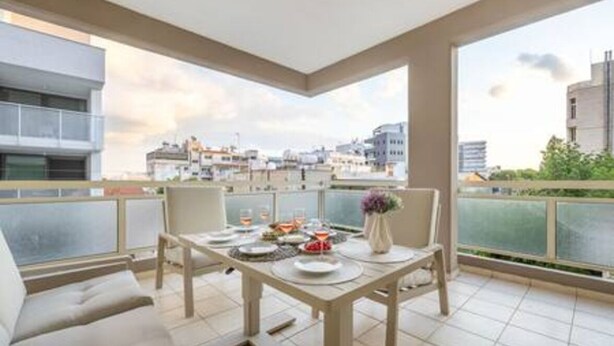 Uma varanda com mesa de jantar posta para dois, um sofá e vista para a cidade.