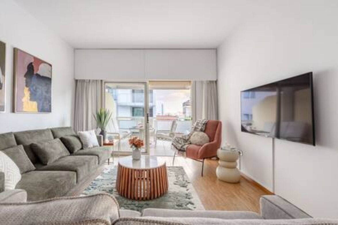 A modern living room with a sofa, armchair, coffee table, and a flat-screen TV mounted on the wall.