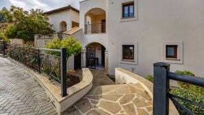 A two-story building with a stone pathway, a balcony, and a small garden area. - BK02 Adjacent to Aphrodite Hills – Pool & Sea View (Kouklia)