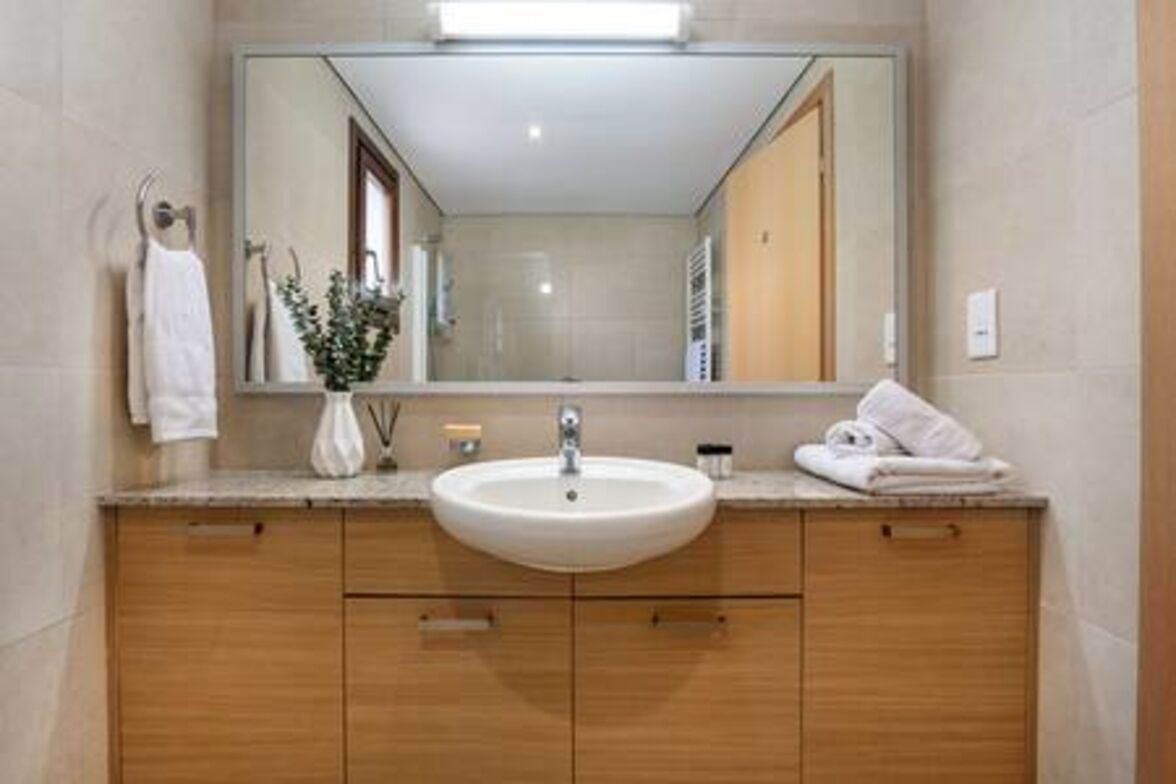 A bathroom with a large mirror, a sink, wooden cabinets, and a towel rack.