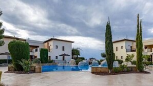 A resort with a swimming pool, multiple buildings, and a clear sky. - BK02 Adjacent to Aphrodite Hills – Pool & Sea View (Kouklia)