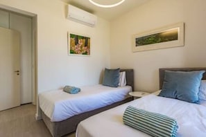 Een hotelkamer met twee bedden, een nachtkastje, een airconditioning en een fotokader aan de muur.