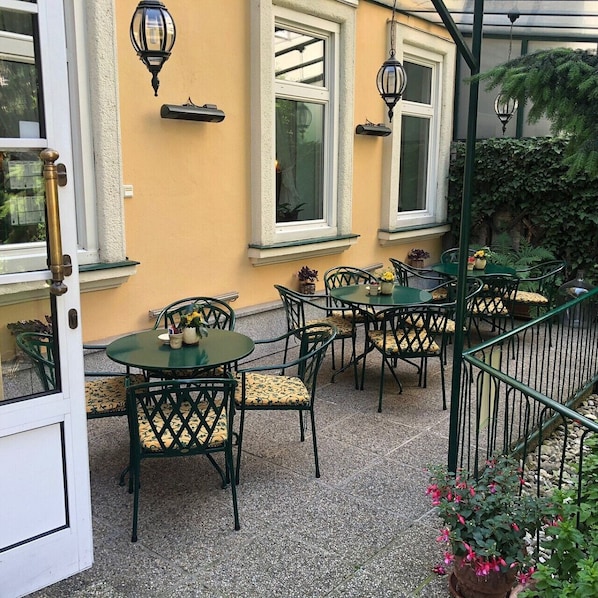 An outdoor patio with tables and chairs, a door, and a wall-mounted light fixture. - defaultName (Wien)