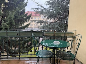 A balcony with a green metal table and chairs, overlooking a building with a red roof and trees. - defaultName (Wien)