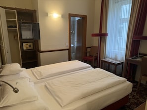 A hotel room with two beds, a wardrobe, a desk, and a shower area. - defaultName (Wien)