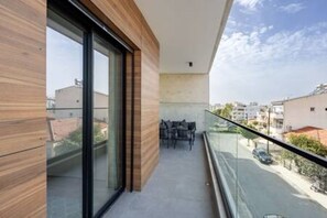 A modern balcony with a glass railing, a wooden wall, and a view of the street below.