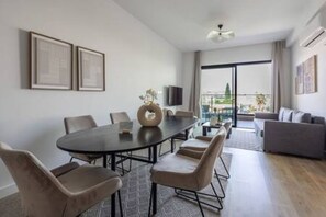 Uma sala de estar moderna com uma mesa de jantar redonda, assentos confortáveis, uma televisão de tela plana e uma grande janela com vista para a cidade.