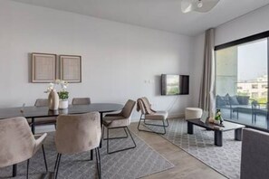 Un salon moderne comprenant une table à manger, des sièges confortables, un téléviseur à écran plat et de grandes fenêtres offrant une vue dégagée.