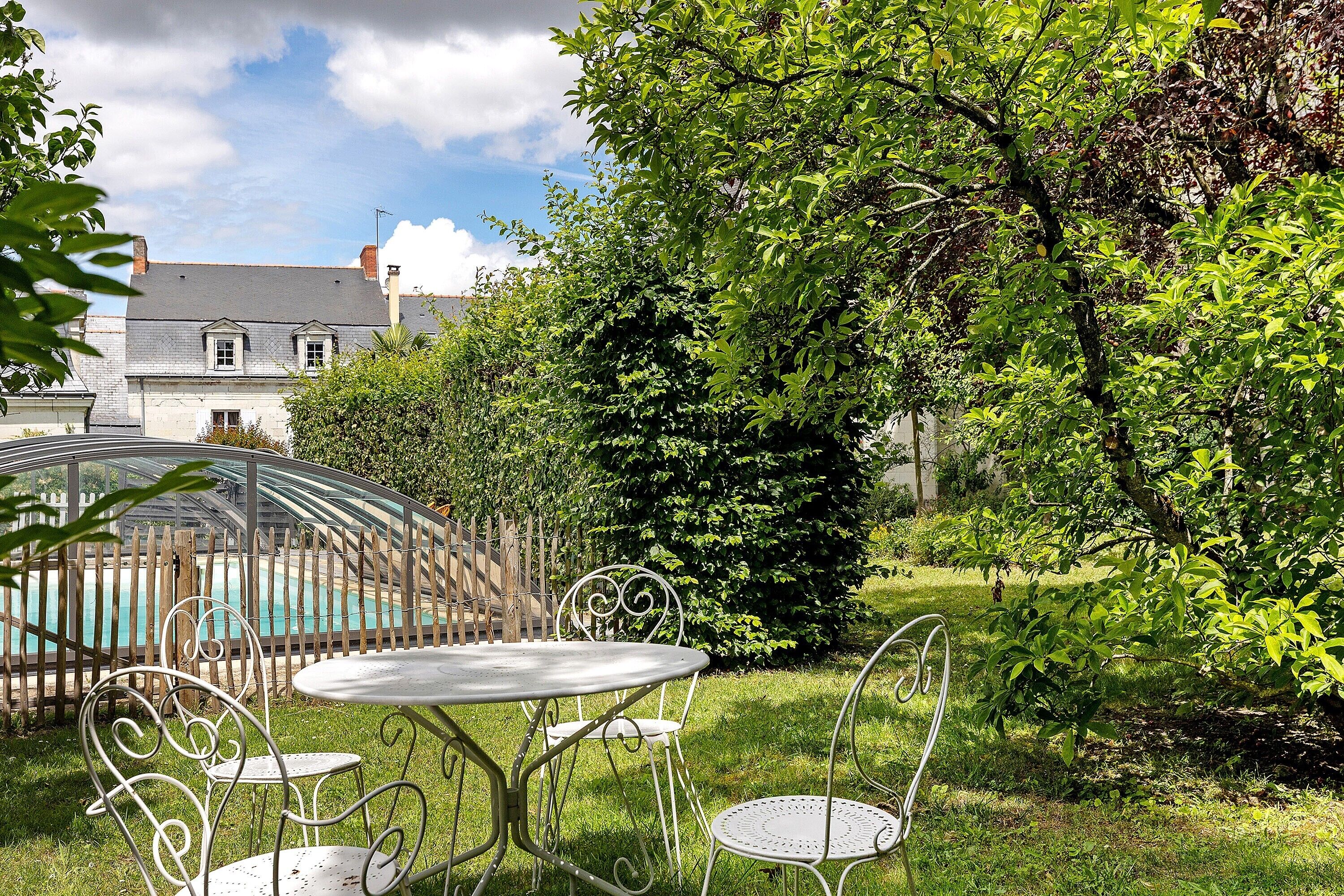 Un jardin avec une table et des chaises en métal, une piscine et une maison en arrière-plan.