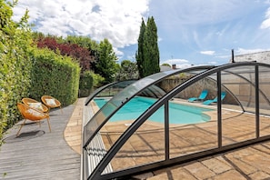 Un espace piscine doté d’une enceinte en verre, d’une terrasse en bois et de mobilier d’extérieur.