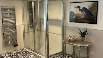 A bathroom with a glass shower enclosure, a tiled floor, a sink with a decorative bowl, and a framed picture on the wall.